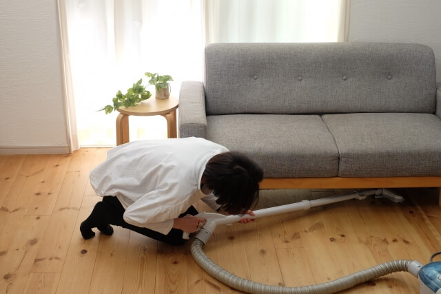 ソファの下を掃除する女性
